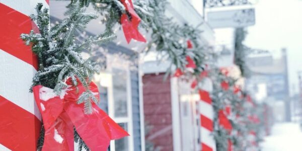 Small shopping chalets are decorated with pine and red ribbon. Snow frosts the decor.