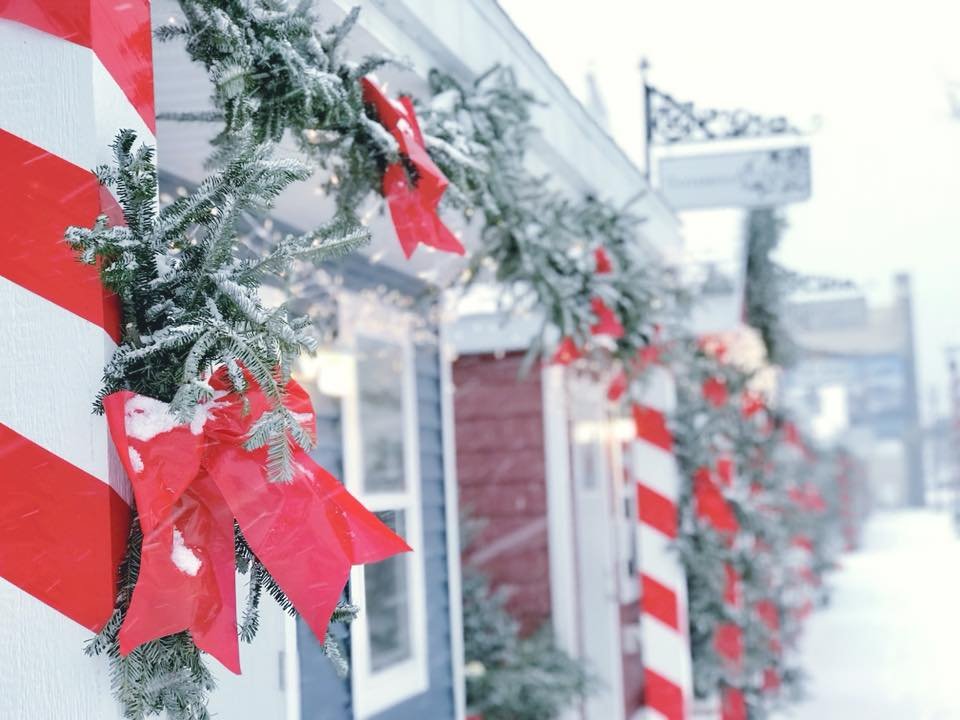 Small shopping chalets are decorated with pine and red ribbon. Snow frosts the decor.