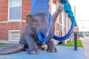 6 foot bonze statue of mastodon with large bright blue tusks in front of museum