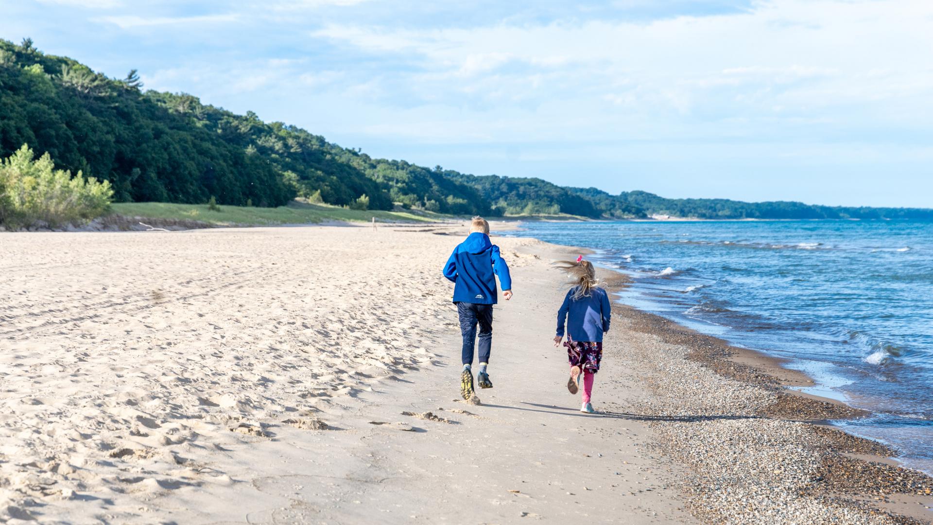 young children running up the coastline of lake michigan