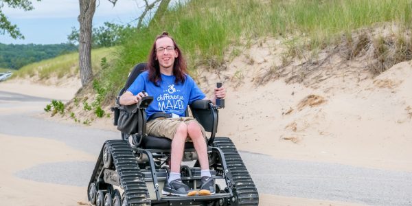 TrackChair Muskegon State Park Beach Person in a motorized all-terrain wheelchair smiling while traversing a sandy dune at Muskegon State park