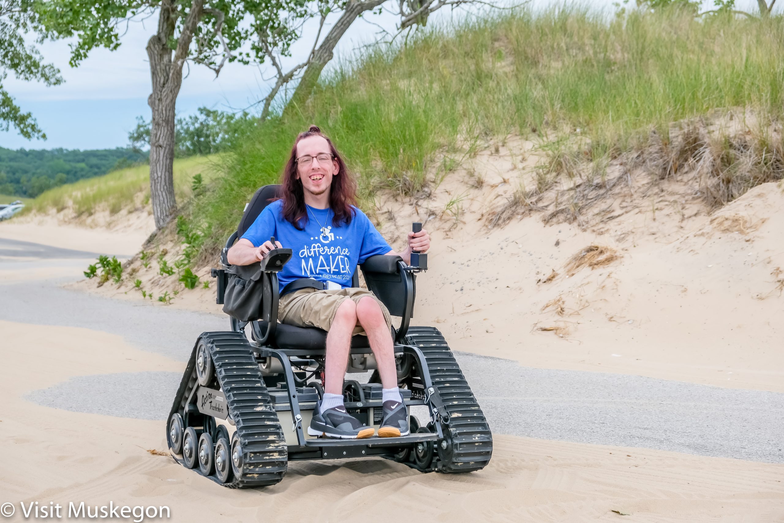 Person in a motorized all-terrain wheelchair smiling while traversing a sandy dune at Muskegon State park