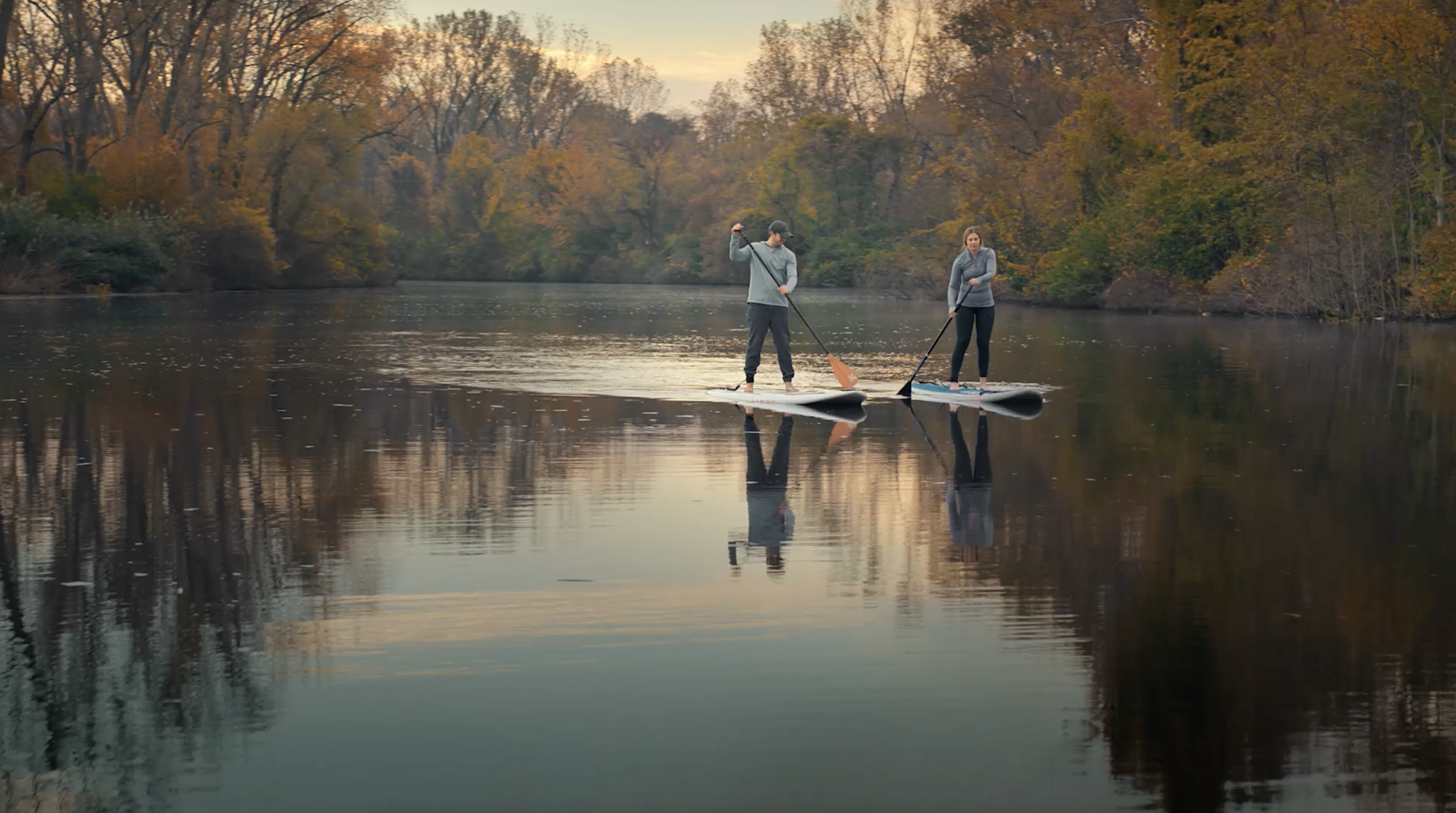  Two people paddleboard on a calm river surrounded by colorful autumn trees in Southwest Michigan.